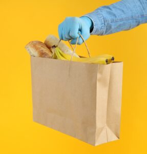 Hand in gloves hold bag with food on yellow background